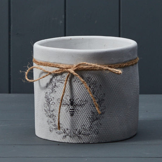 Decorative pot with a textured design and twine bow on a dark wooden surface.